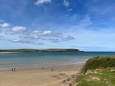 A beach with people walking along the shore and an island in the distance at Obos Retreat in St Minver near Rock