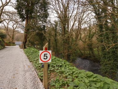 A gravel road with a speed limit sign near a river and trees at Primrose in Hellandbridge near Bodmin