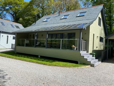 A modern house with a glass railing porch and steps on a gravel driveway surrounded by grass at Primrose Hellandbridge near Bodmin