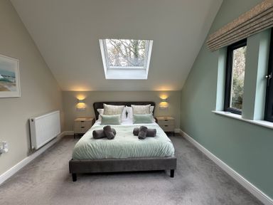 A bedroom with a bed under a skylight window and two side tables with lamps at Primrose in Hellandbridge near Bodmin