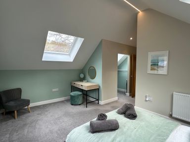 A bedroom with a skylight window a green and beige wall a gray chair and a vanity table with a round mirror at Primrose in Hellandbridge near Bodmin