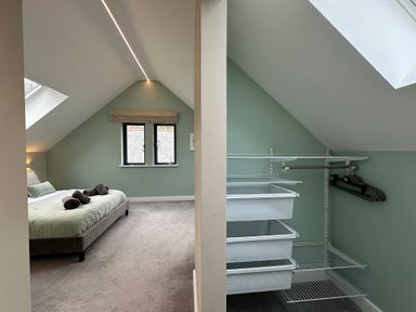 A bedroom with a bed and towels next to a walk in closet with shelves and hangers at Primrose in Hellandbridge near Bodmin