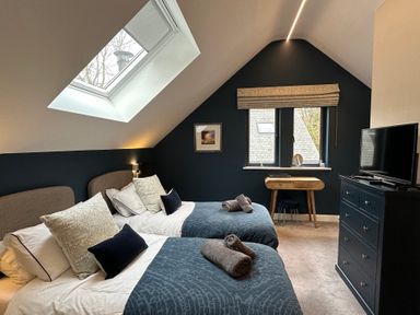 A bedroom with two beds a skylight a window a wooden desk and a dresser with a television at Primrose in Hellandbridge near Bodmin