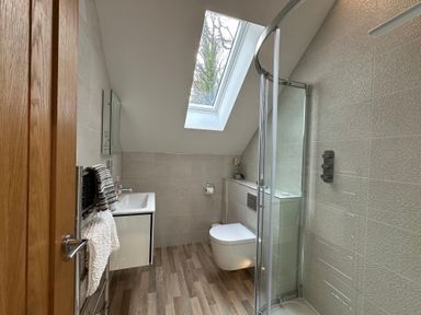 A bathroom with a skylight window a wall-mounted toilet a shower enclosure a sink with a mirror and towels at Primrose in Hellandbridge near Bodmin