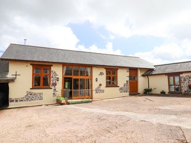 A courtyard with a barn building featuring wooden windows and doors at Quoit X Barn in Stoodleigh near Bampton