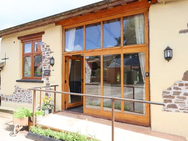 Exterior view of a barn with large wooden framed glass doors and windows at Quoit X Barn in Stoodleigh near Bampton