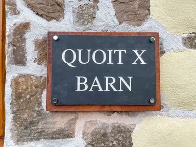 A stone wall with a black and brown sign reading Quoit X Barn