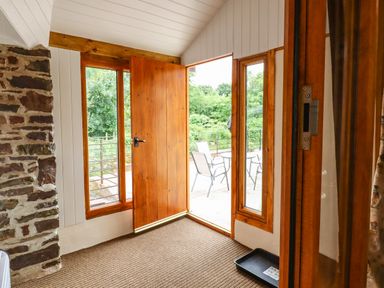 An entryway with a wooden door open to a patio with outdoor chairs and a table at Quoit X Barn in Stoodleigh near Bampton