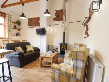 A living room with leather sofa armchairs a wood stove and a wooden coffee table at Quoit X Barn Stoodleigh near Bampton