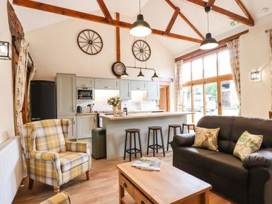 An open living room and kitchen with a plaid armchair black sofa and wooden coffee table at Quoit X Barn in Stoodleigh near Bampton