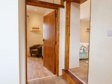 A hallway leading to a room with a brown chair and coat hangers and another room with a bed partially visible at Quoit X Barn in Stoodleigh near Bampton
