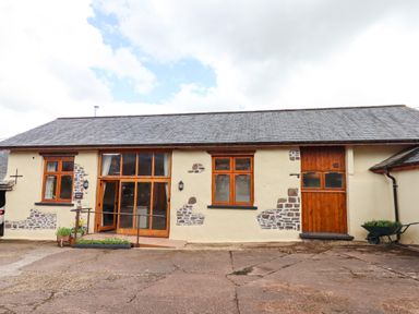 An exterior view of a barn with wooden windows and doors with stone patches on the walls at Quoit X Barn Stoodleigh near Bampton