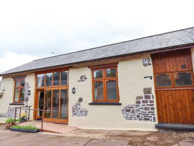 Exterior view of a single story building with wooden framed windows and door at Quoit X Barn in Stoodleigh near Bampton