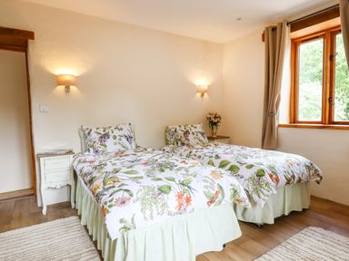 A bedroom with two single beds with floral bedspreads and bedside tables at Quoit X Barn in Stoodleigh near Bampton