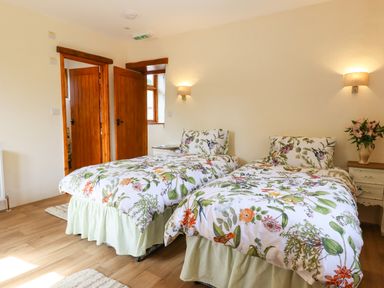 A bedroom with two single beds with floral bedding and wooden doors at Quoit X Barn in Stoodleigh near Bampton