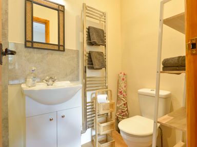 A bathroom with a sink cabinet mirror towel rack and toilet with shelves holding towels at Quoit X Barn in Stoodleigh near Bampton