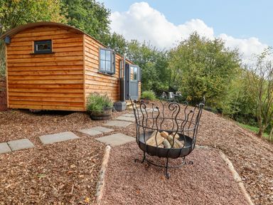 A wooden cabin with a fire pit and outdoor seating in a garden at Hideaway Cabin in Cadbury near Thorverton