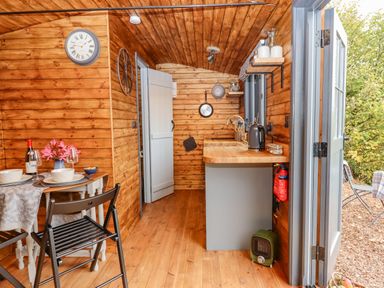 A small wooden kitchen and dining area with a table set for two and an open door leading outside at Hideaway Cabin in Cadbury near Thorverton