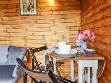 A small dining table set with bowls glasses and flowers next to wooden walls and black chairs at Hideaway Cabin in Cadbury near Thorverton
