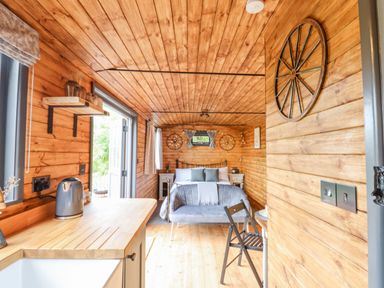 A wooden interior room with a bed a small sofa a kitchen counter with a kettle and a folding chair at Hideaway Cabin in Cadbury near Thorverton