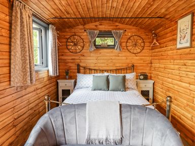 A bedroom with a bed between two nightstands and a chair facing the bed at Hideaway Cabin in Cadbury near Thorverton