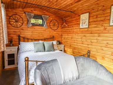A bedroom with a double bed two bedside tables a small window and a gray sofa at Hideaway Cabin in Cadbury near Thorverton