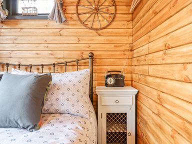 A wooden bedroom with a metal framed bed pillows a bedside table and a vintage radio at Hideaway Cabin in Cadbury near Thorverton