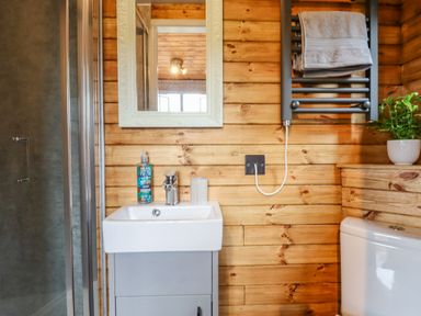 A bathroom with wooden walls a sink with a mirror above a toilet and a towel rack at Hideaway Cabin in Cadbury near Thorverton