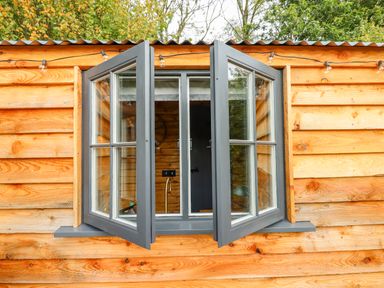 An open window with grey frames on a wooden cabin wall at Hideaway Cabin in Cadbury near Thorverton