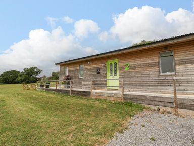 A wooden cabin with a green door and number 2 on the wall with chairs and plants on a grassy area at Lulu Logs in Congresbury