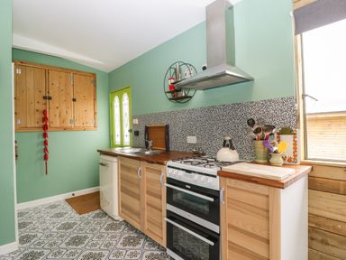 A kitchen with wooden cabinets a gas stove a sink and a patterned floor at Lulu Logs in Congresbury