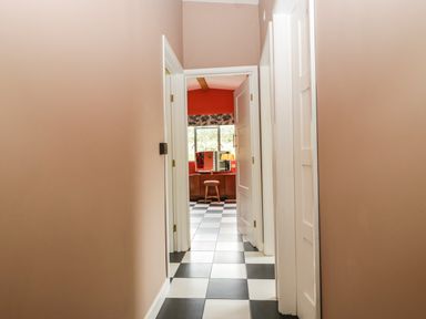 A hallway with checkered black and white floor tiles leading to a room with a wooden dresser stool and window at Lulu Logs in Congresbury