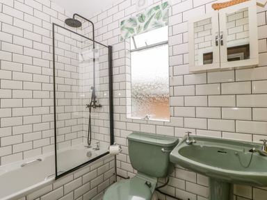 A bathroom with a green toilet and sink a bathtub with a shower and tiled walls at Lulu Logs in Congresbury