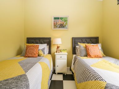 A bedroom with two single beds a white nightstand with a lamp and books and a painting on the wall at Lulu Logs in Congresbury