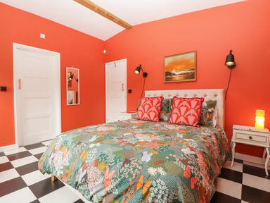 A bedroom with a double bed with floral and butterfly patterned bedding red walls black and white checkered floor at Lulu Logs in Congresbury