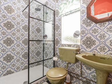A bathroom with patterned wall tiles a green toilet and sink and a glass shower enclosure at Lulu Logs in Congresbury