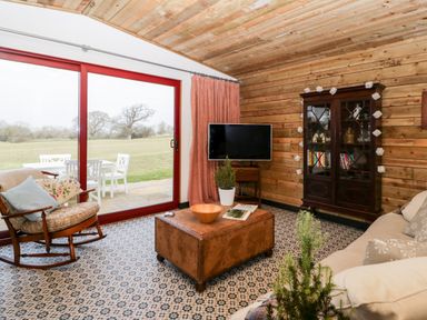 A living room with a rocking chair a sofa a wooden coffee table a TV cabinet and large patio doors at Down the Rabbit Hole Brinsea near Congresbury