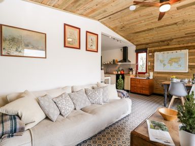 A living room with a beige sofa and patterned cushions next to a kitchen and dining area with wooden ceiling at Down the Rabbit Hole Brinsea near Congresbury