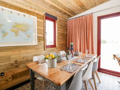 A dining room with a wooden table set with placemats glasses and decor items and white chairs at Down the Rabbit Hole in Brinsea near Congresbury