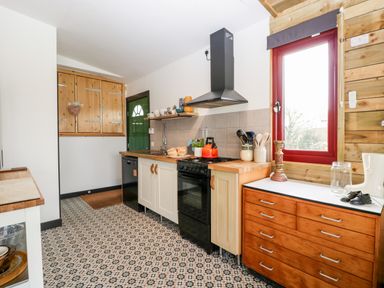 A kitchen with wooden cabinets a patterned tiled floor a red window and a green door at Down the Rabbit Hole in Brinsea near Congresbury