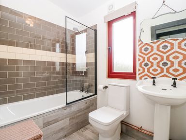 A bathroom with a bathtub shower with tiled walls a toilet a pedestal sink and a window with a red frame at Down the Rabbit Hole Brinsea near Congresbury