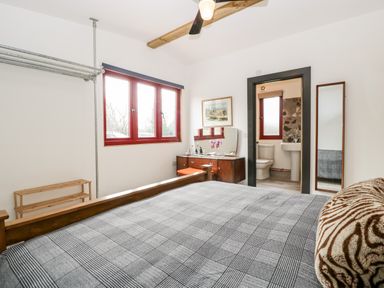 A bedroom with a bed a dressing table a full length mirror a window and an en suite bathroom at Down the Rabbit Hole in Brinsea near Congresbury