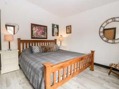 A bedroom with a wooden bed frame gray bedding two nightstands two lamps and three wall art pieces at Down the Rabbit Hole in Brinsea near Congresbury