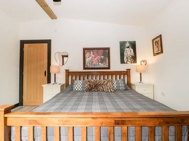 A bedroom with a wooden bed frame gray bedspread pillows and framed pictures on the wall at Down the Rabbit Hole Brinsea near Congresbury