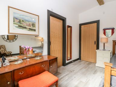 A bedroom with a wooden dresser and orange bench an armchair wooden doors and a nightstand with a lamp at Down the Rabbit Hole in Brinsea near Congresbury