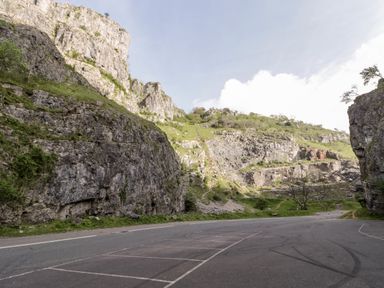 A rocky limestone cliff with greenery and an empty parking area at Down the Rabbit Hole Brinsea near Congresbury