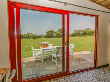 A patio table with chairs and a basket outside on a tiled patio behind a large red-framed glass sliding door at Down the Rabbit Hole in Brinsea near Congresbury