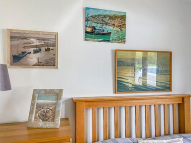 A bedroom wall with three framed paintings above a wooden headboard and a bedside table with a lamp and a framed photo at Down the Rabbit Hole in Brinsea near Congresbury