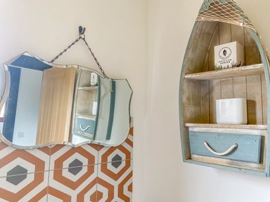A wall with a wavy hanging mirror and a boat-shaped wooden shelf with a drawer and items at Down the Rabbit Hole Brinsea near Congresbury