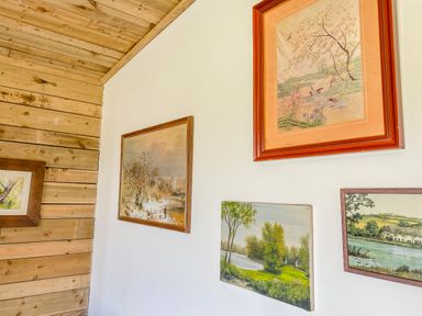 A wall with four framed paintings of nature scenes and a wooden paneled wall at Down the Rabbit Hole Brinsea near Congresbury